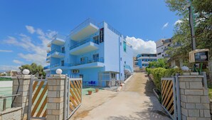 A multi-story hotel with a blue exterior, a gated entrance, and a clear sky. - Esmerald Hotel (Ksamil)