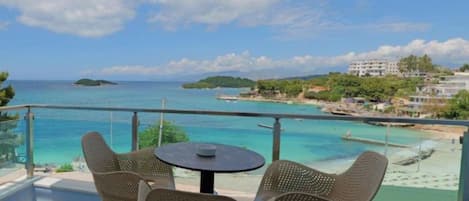 A balcony with a table and chairs overlooking a beach and ocean.