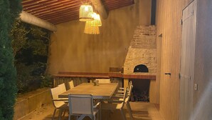 An outdoor patio with a wooden table and chairs, a stone fireplace, and hanging lights. - Superb villa in Puyvert Air conditioning, heated swimming pool, fully enclosed garden (Puyvert)