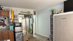 A compact kitchen with a microwave, toaster, and washing machine. A small plant is on the floor, and a surfboard decoration hangs on the wall. - BEACH GETAWAY!! 🏖🏖🏖 (Wildwood Crest)
