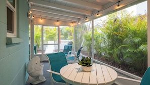 Un patio techado con una mesa redonda, sillas y una planta en maceta.