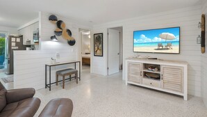 Una sala de estar moderna con televisor, ventilador de techo y un cuadro con motivos playeros.