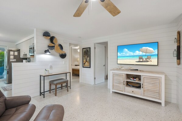 A modern living room with a TV, a ceiling fan, and a beach-themed painting.