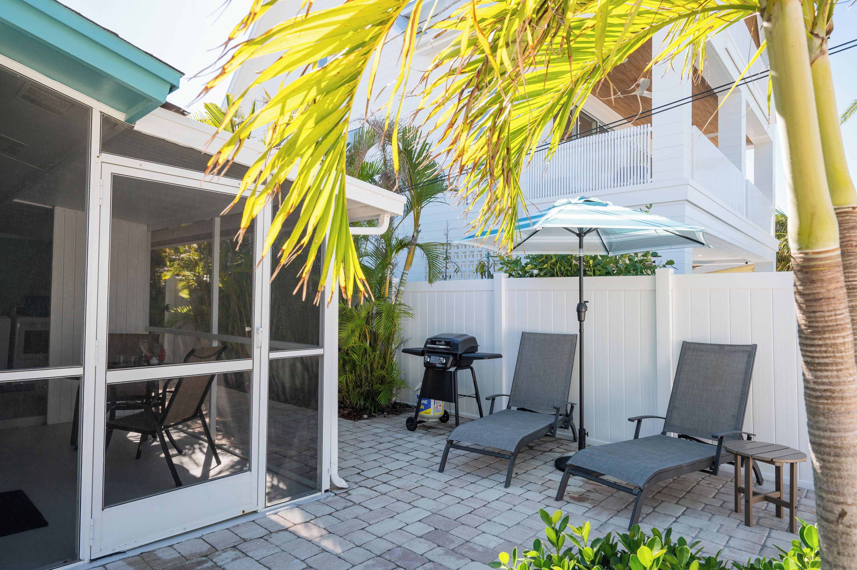 A patio with a covered seating area, a grill, and a white fence.