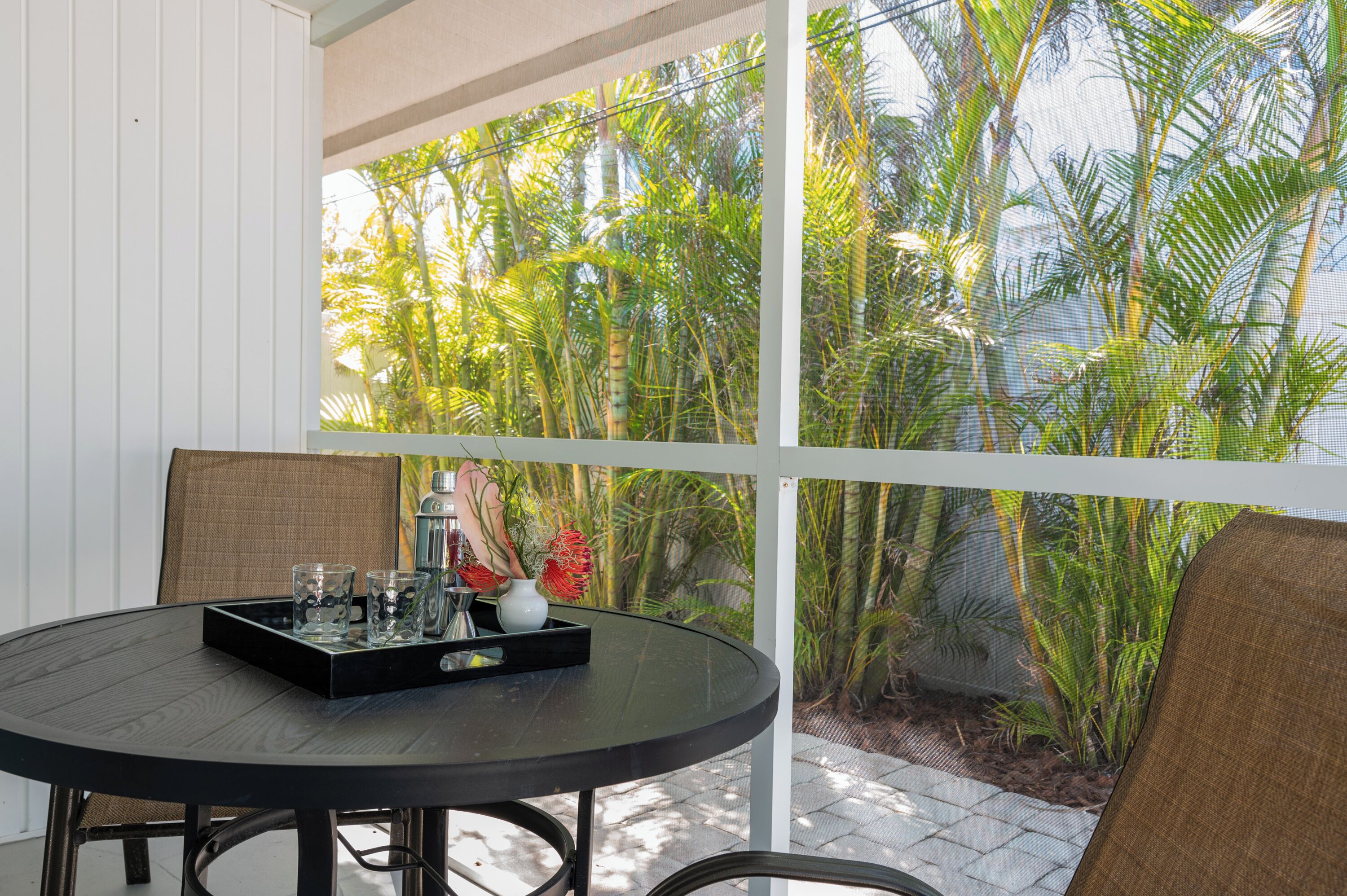 A round table with a tray, glasses, and a water bottle, set against a backdrop of lush tropical plants and a white wall.
