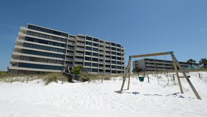Um hotel na praia com vários andares, uma praia de areia em primeiro plano e um balanço.