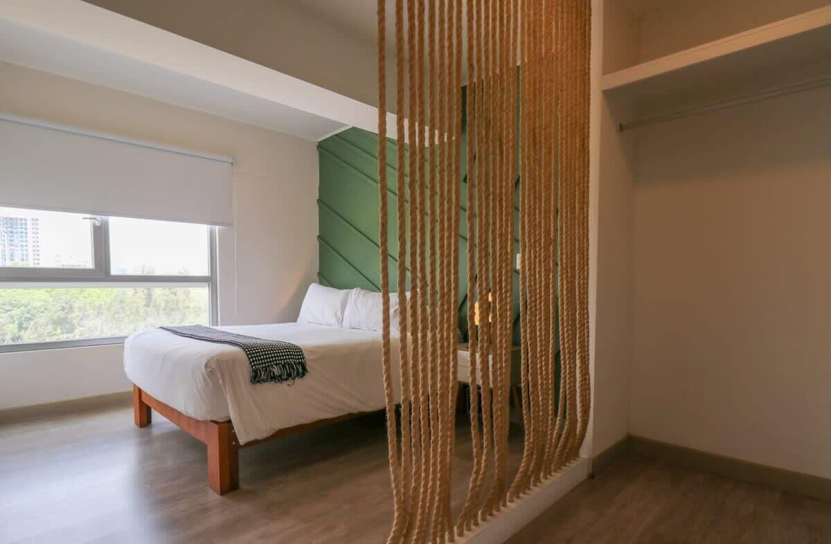 Ein Schlafzimmer mit einem Bett, einem grünen Kopfteil und Blick ins Freie.