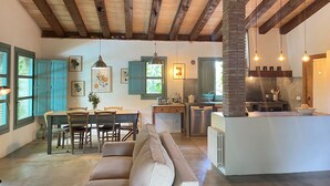 Un vaste espace de vie doté d’un plafond en bois, d’une table à manger avec des chaises, d’un canapé et d’un coin cuisine équipé d’un évier et d’une cuisinière.