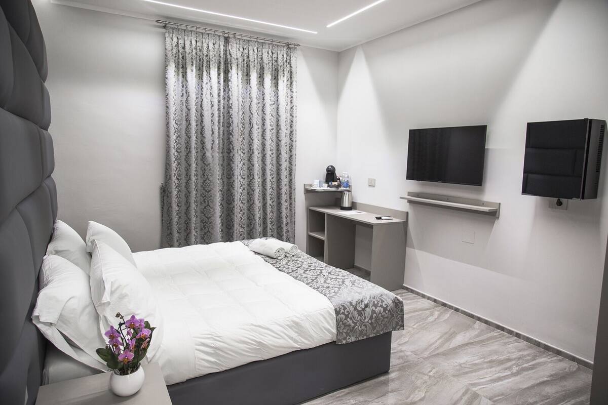 Een moderne hotelkamer met een groot bed, een bureau, een flatscreen televisie en een kamerplant.