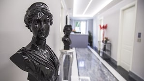 Un couloir avec un buste sculpté sur la gauche, une statue au centre et une porte sur la droite.