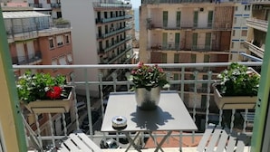 Un balcon avec une table et des plantes en pot, donnant sur un quartier résidentiel composé d’immeubles à plusieurs étages.