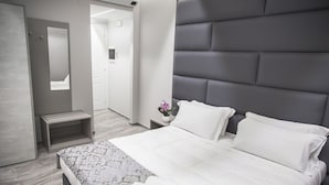 Une chambre d’hôtel moderne avec un grand lit, une table de chevet, un miroir et un petit banc.
