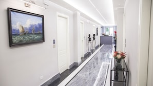 Un couloir d’hôtel moderne avec un sol en marbre, un tableau encadré représentant un navire sur le côté gauche, et un comptoir d’accueil au fond.
