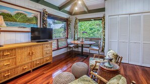 Una habitación con un armario de madera, televisor, mesa de comedor con sillas y vista a la vegetación a través de una ventana.