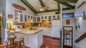 Una cocina con gabinetes blancos, una isla de madera con taburetes, un letrero con forma de tabla de surf y un letrero de precaución.