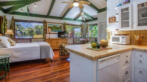 Una habitación con cama, mesa de comedor, zona de cocina y un ventanal con vistas a zonas verdes.