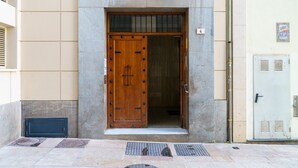 A wooden door with a metal grill, a small step leading up to it, and a metal vent on the adjacent wall. - MalagaSuite Cathedral Center (Málaga)