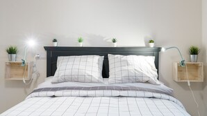 A neatly made bed with a grid-patterned duvet, bedside tables with potted plants, and a wall-mounted lamp. - MalagaSuite Cathedral Center (Málaga)