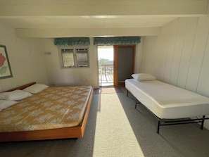 Una habitació amb un llit, un llit més petit, una finestra i una porta que dóna a un espai exterior.