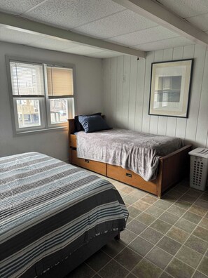 A bedroom with two beds, a wooden dresser, a framed picture on the wall, and a laundry basket. - Oceanfront 3 Bedroom 3 Bath Vacation Rental in Ocean City MD | Direct Beach Access, Sealax Awhile (Ocean City)