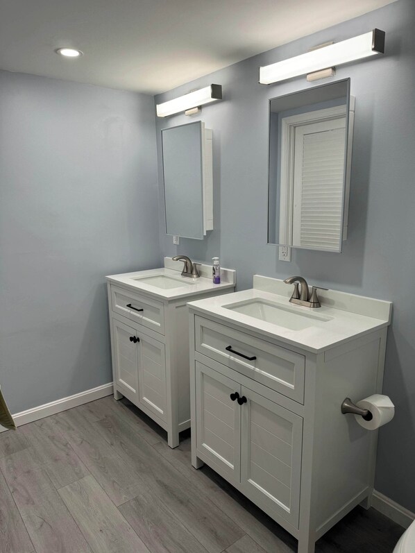 Une salle de bain avec deux lavabos, un miroir au-dessus de chacun, et des toilettes dotées d’un porte-serviettes en papier.