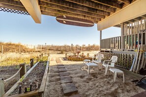 A covered outdoor area with a sandy floor, a wooden deck, and a seating area with white plastic chairs. - Oceanfront 3 Bedroom 3 Bath Vacation Rental in Ocean City MD | Direct Beach Access, Sealax Awhile (Ocean City)