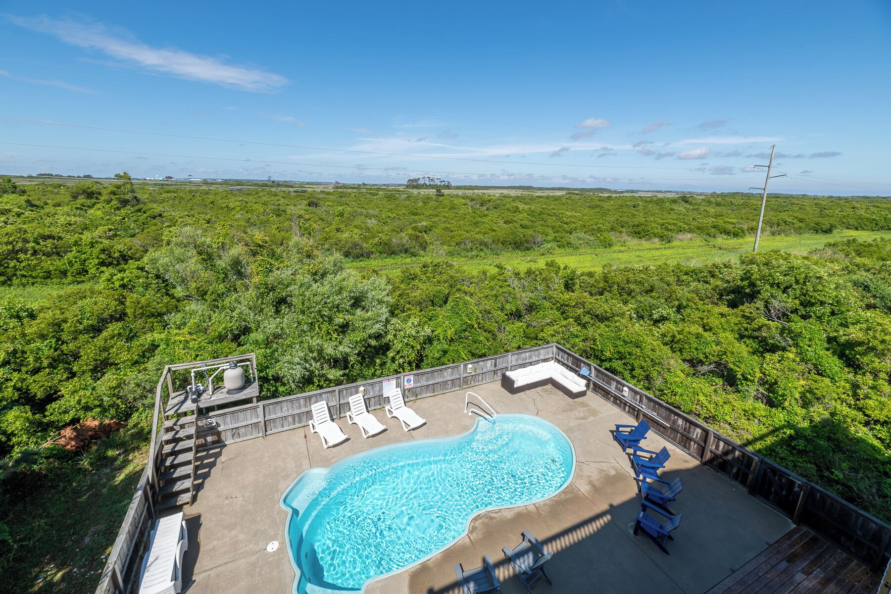 Une piscine entourée d’une végétation luxuriante, avec des chaises longues et une terrasse en bois.