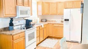 A kitchen with wooden cabinets, a microwave, stove, refrigerator, and a ceiling fan. - Cottage 304, 2 Bed w/ Fire Pit, near trails! (West Logan)
