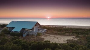 A beachfront property with a blue-roofed building, a wooden deck, and a view of the ocean at sunset. - Edisto 1BR w/Beach Access & Resort Amenities (Edisto Island)