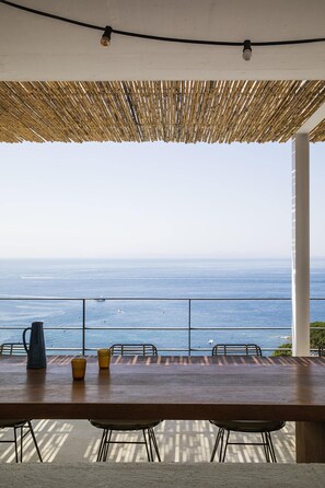 Een terras met een uitzicht op de oceaan, een rieten dak en een tafel met stoelen.