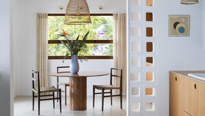 A dining area with a round wooden table, two chairs, a vase with flowers, a hanging pendant light, and a window with curtains. - Exclusive & stylish villa. Concierge service included (Roses)