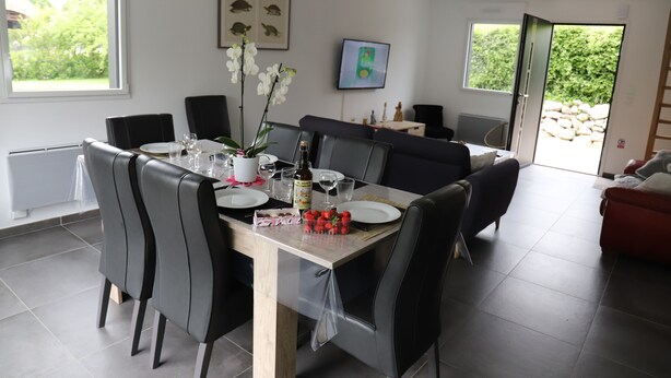 A dining area with a table set for four, surrounded by black chairs. There are plates, glasses, and a bottle on the table. A potted plant with white flowers is on the table.