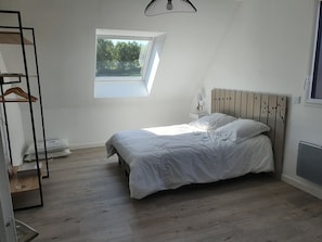 Um quarto com teto inclinado, uma cama com roupa de cama branca, uma pequena janela e um radiador.