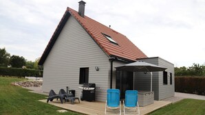 A modern house with a sloped roof, a deck with two blue chairs, a barbecue grill, and a covered patio area.