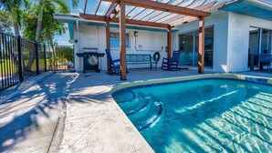 Area piscina con pergola, poltrone relax e patio coperto.