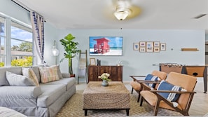A living room with a sofa, armchair, ottoman, and a television displaying a beach scene.