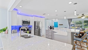 A modern kitchen with white cabinets, stainless steel appliances, and a blue accent wall.