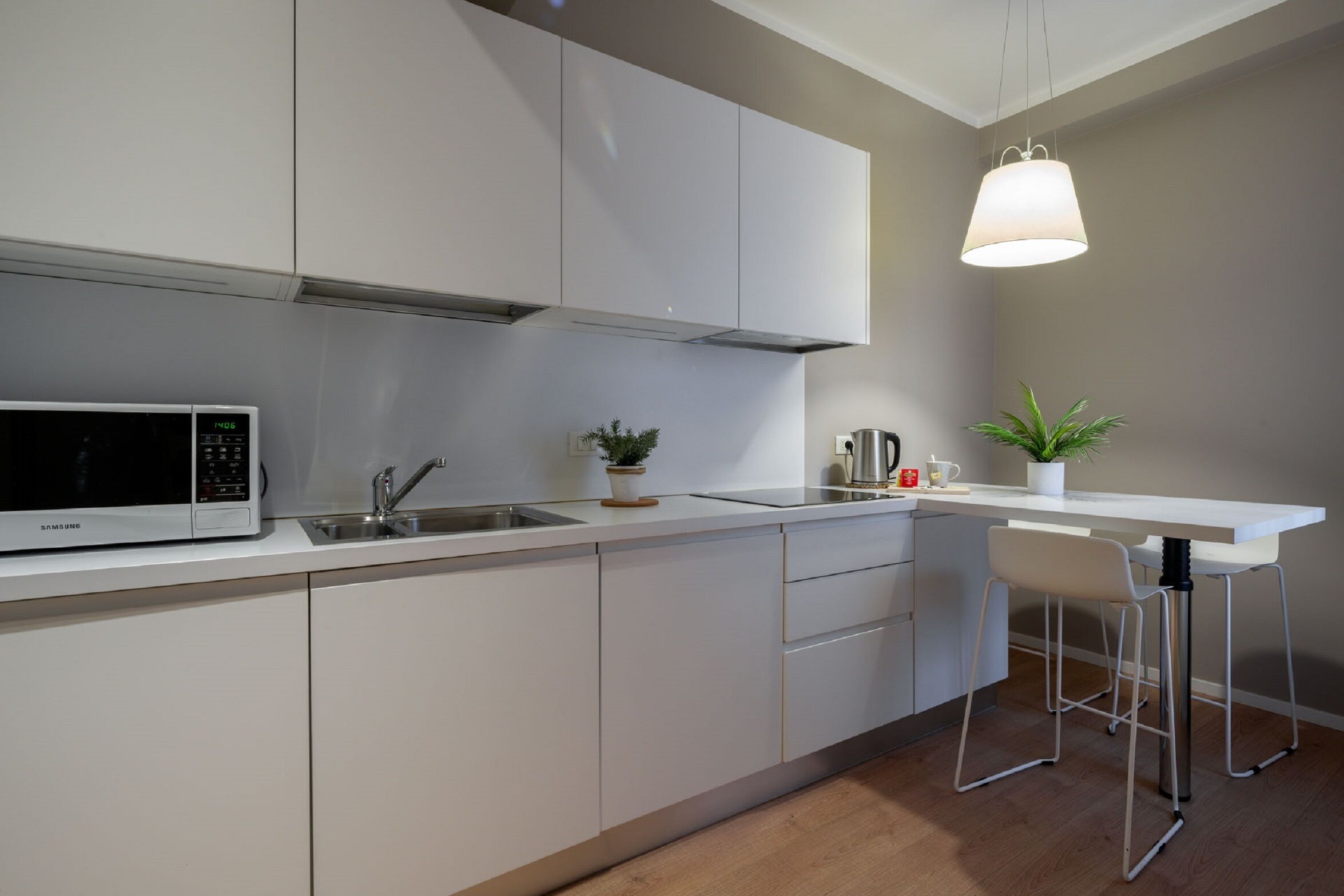 A modern kitchen with white cabinetry, a stainless steel sink, a microwave, and a bar area with stools.