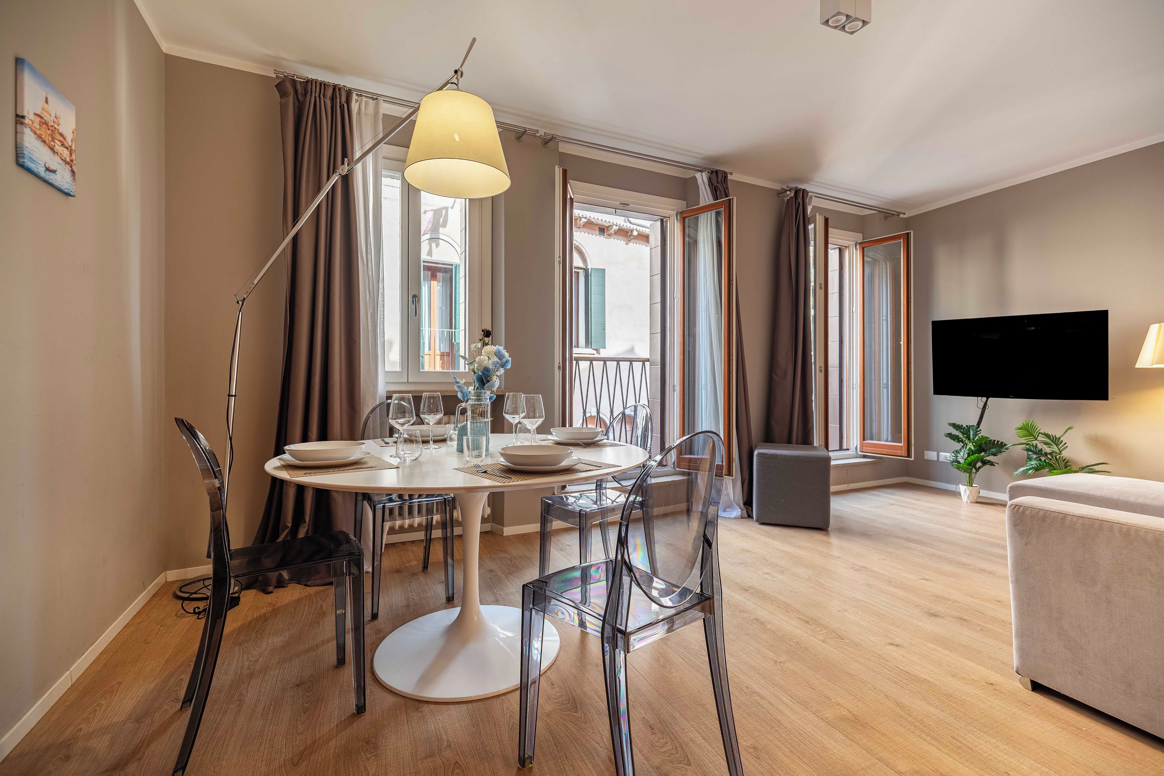 Una sala de estar moderna con comedor, un televisor de pantalla plana y un balcón con cortinas.