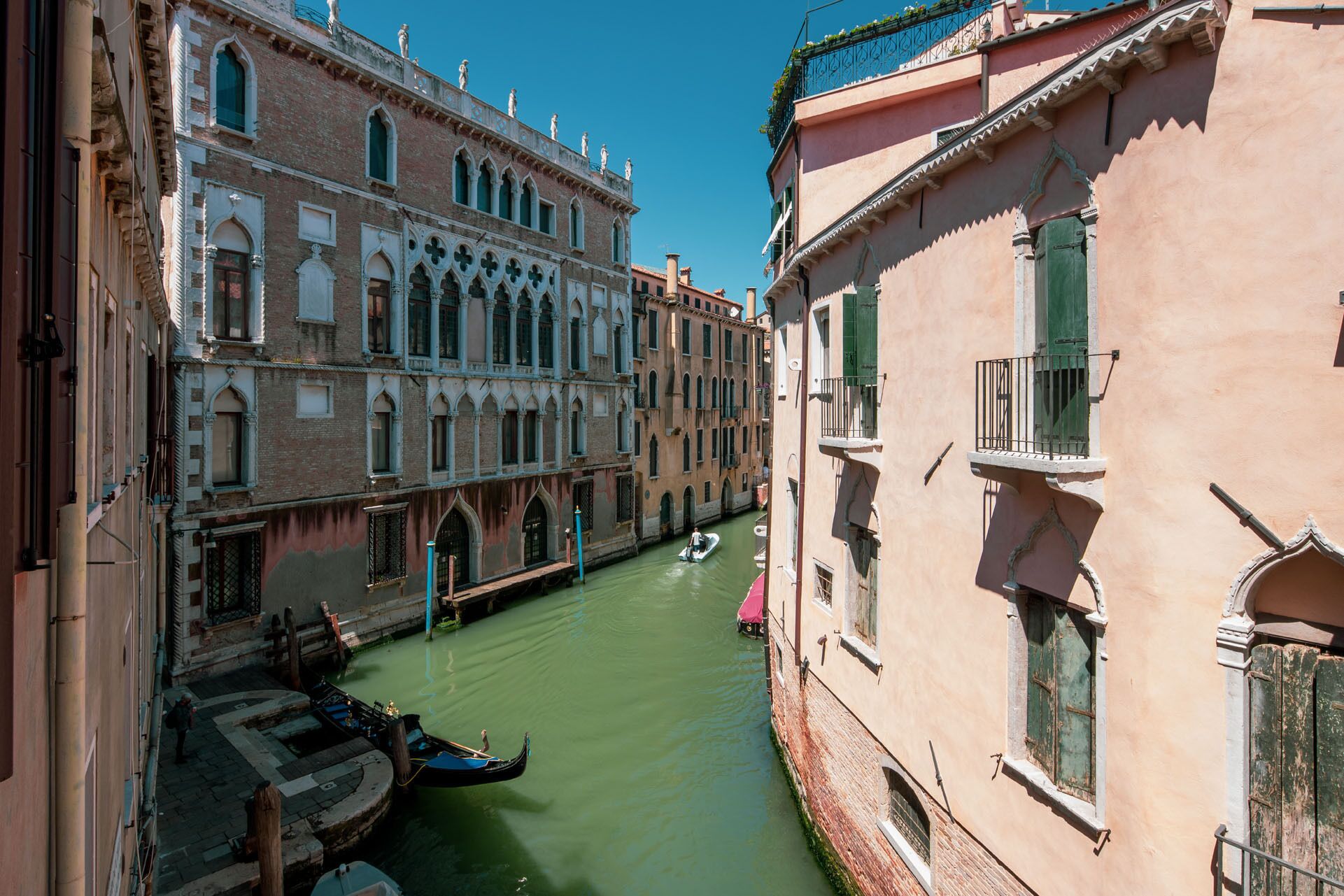 A narrow canal with buildings on either side, a gondola, and a boat in the water.