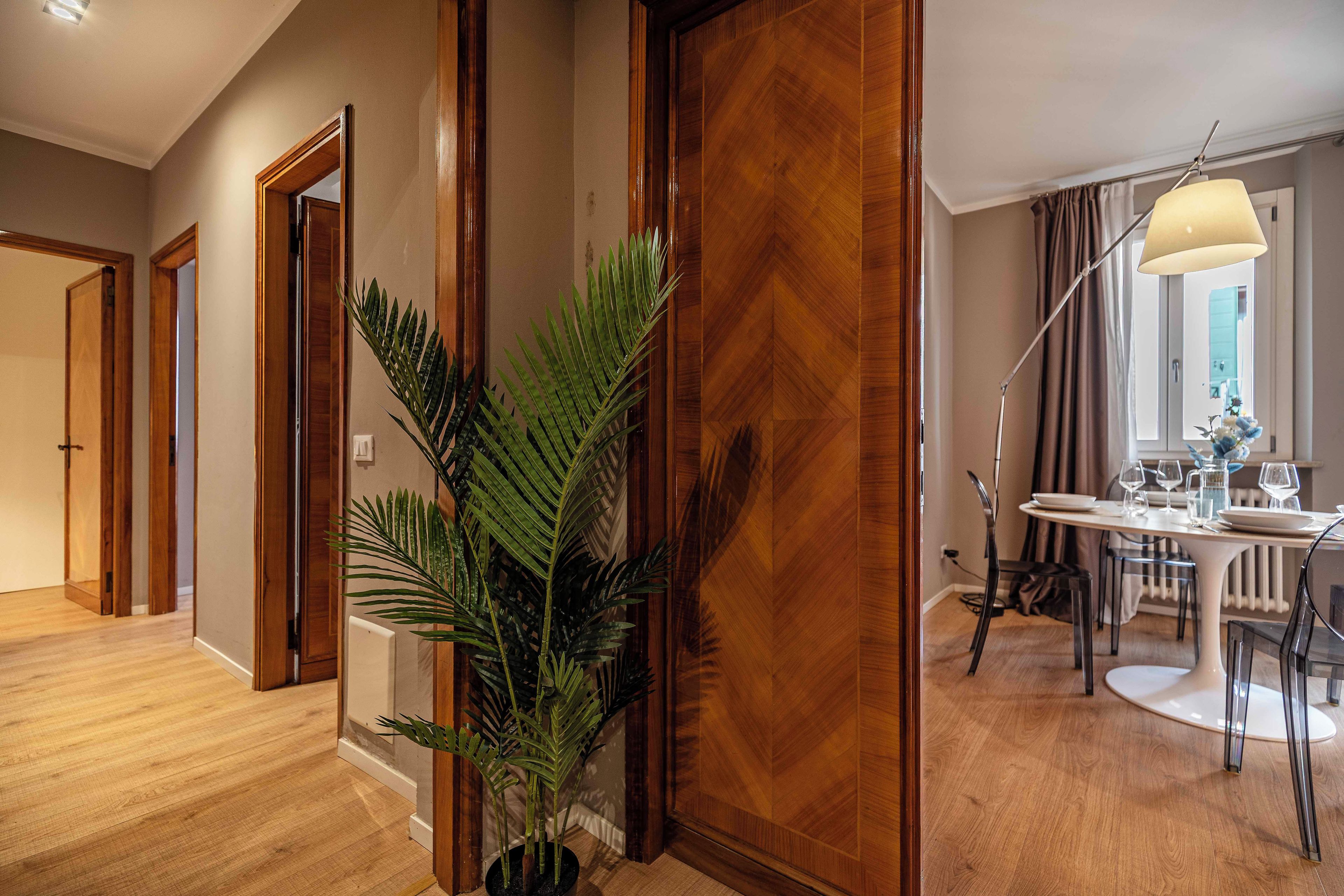 Pasillo de hotel con suelo de madera, una planta en maceta y un comedor con mesa y sillas.