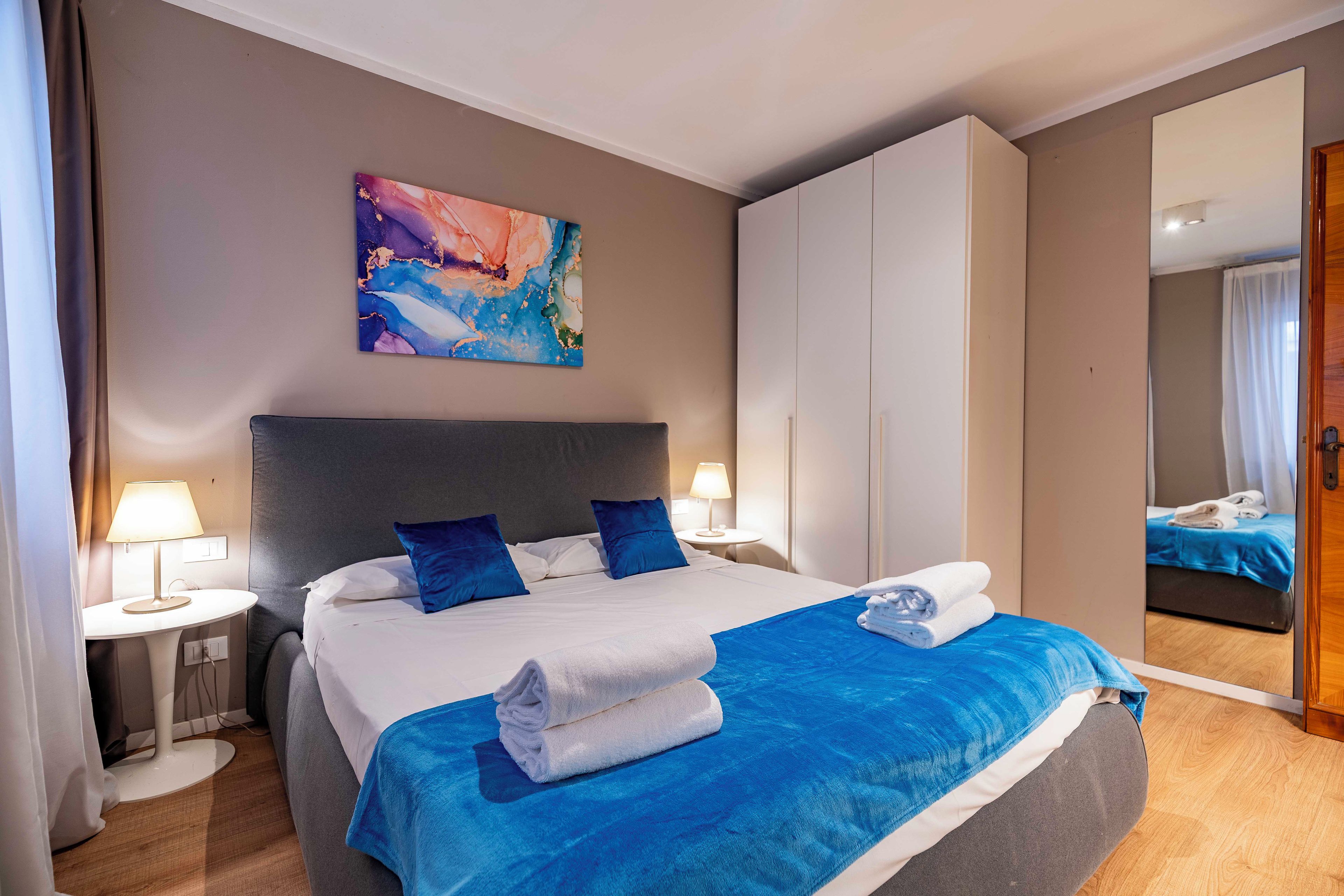 A hotel room with a bed, a painting, a mirror, and a bathroom visible in the reflection.