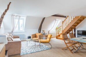 Un loft spacieux avec un plafond haut, un escalier en bois, un canapé, un fauteuil et une table à manger.