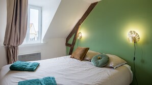 Et soveværelse med skråvæg, en seng med hvide sengetøj, to puder og et turkis plaide.