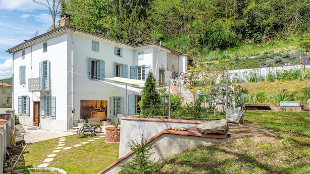 Una casa blanca de dos pisos con un balcón, un camino de piedra que conduce a la entrada y un pequeño jardín.