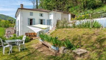 Une maison blanche avec un toit en tuiles, un balcon et une table entourée de chaises dans le jardin.