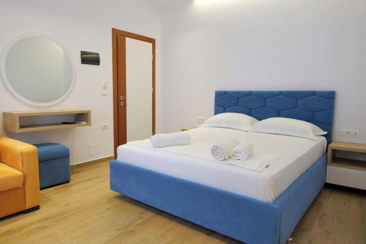 Ein Schlafzimmer mit einem Bett, einem runden Spiegel, einer Holztür und einem blau gepolsterten Sessel.