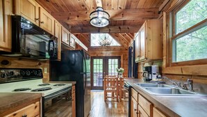 A wooden cabin kitchen with a stove, microwave, refrigerator, and a large window. - Cabin in the Woods w/ Hot Tub (Sevierville)