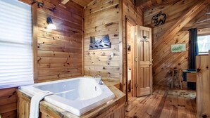 A wooden cabin interior with a large bathtub, wooden walls, a bear decoration, and a small ladder. - Cabin in the Woods w/ Hot Tub (Sevierville)