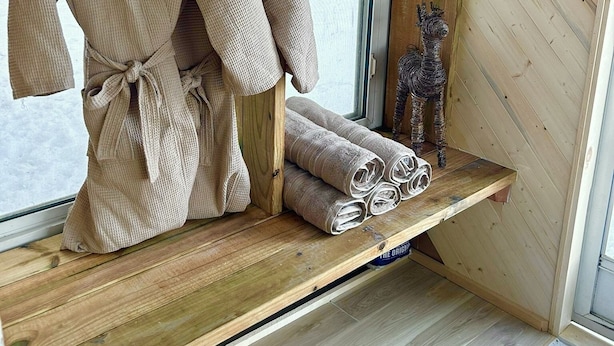 A wooden room with a bathrobe hanging on a rack, a shelf with rolled towels, and a small decorative item. - Cozy Cottage with Pool+Jacuzzi+Sauna+Fire Pit and Reading Nook! (Livingston Manor)